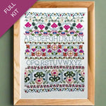 Embroidery kit with floral alphabet design in a wooden frame on a green background