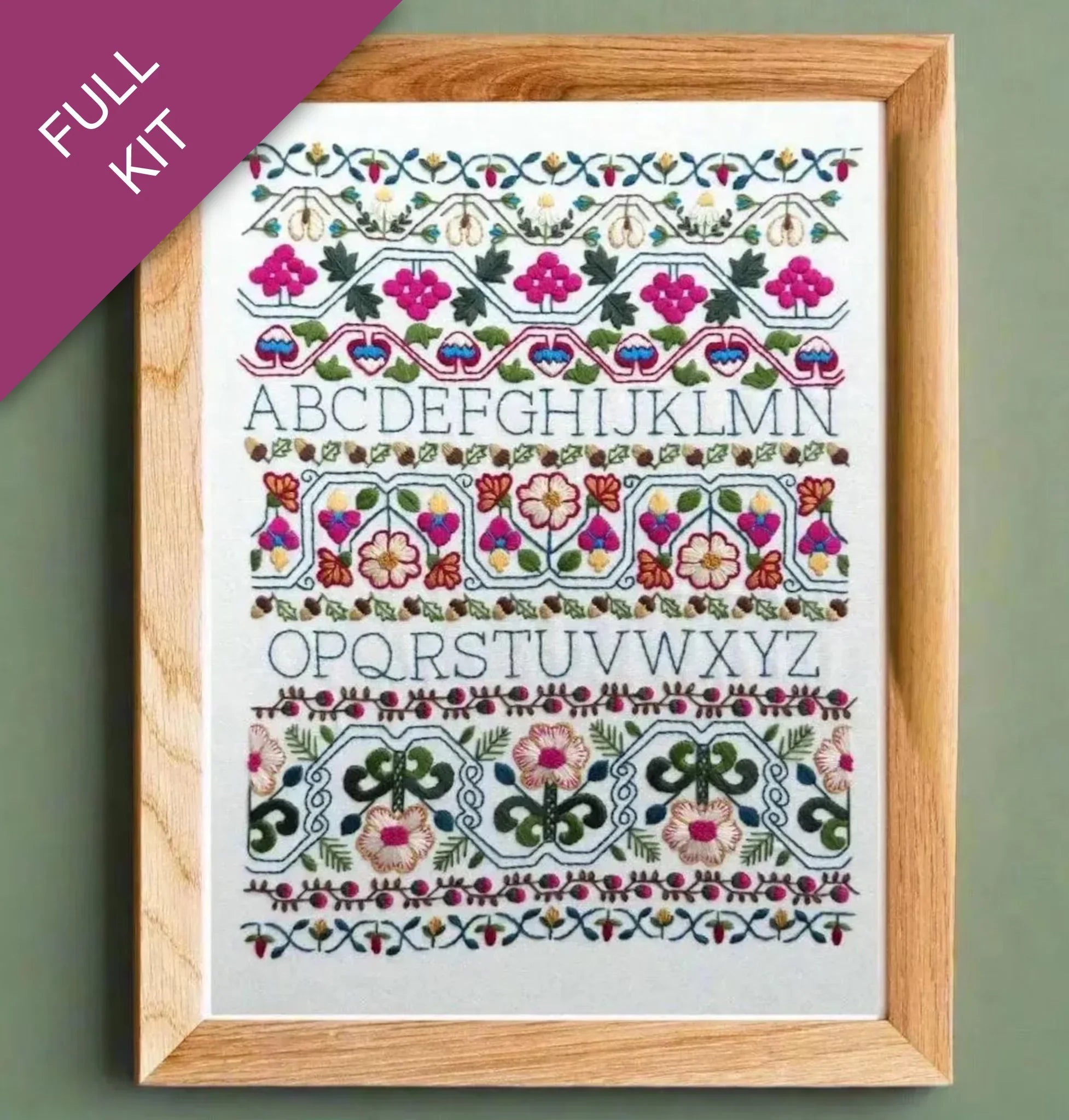 Embroidery kit with floral alphabet design in a wooden frame on a green background