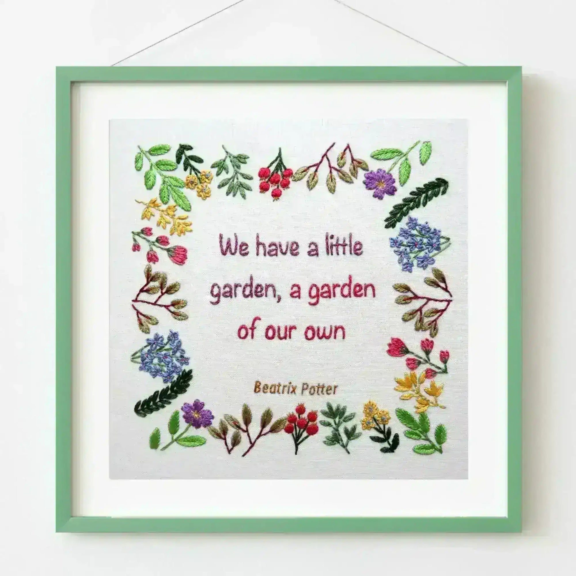 Framed embroidery with floral designs and text on a white background