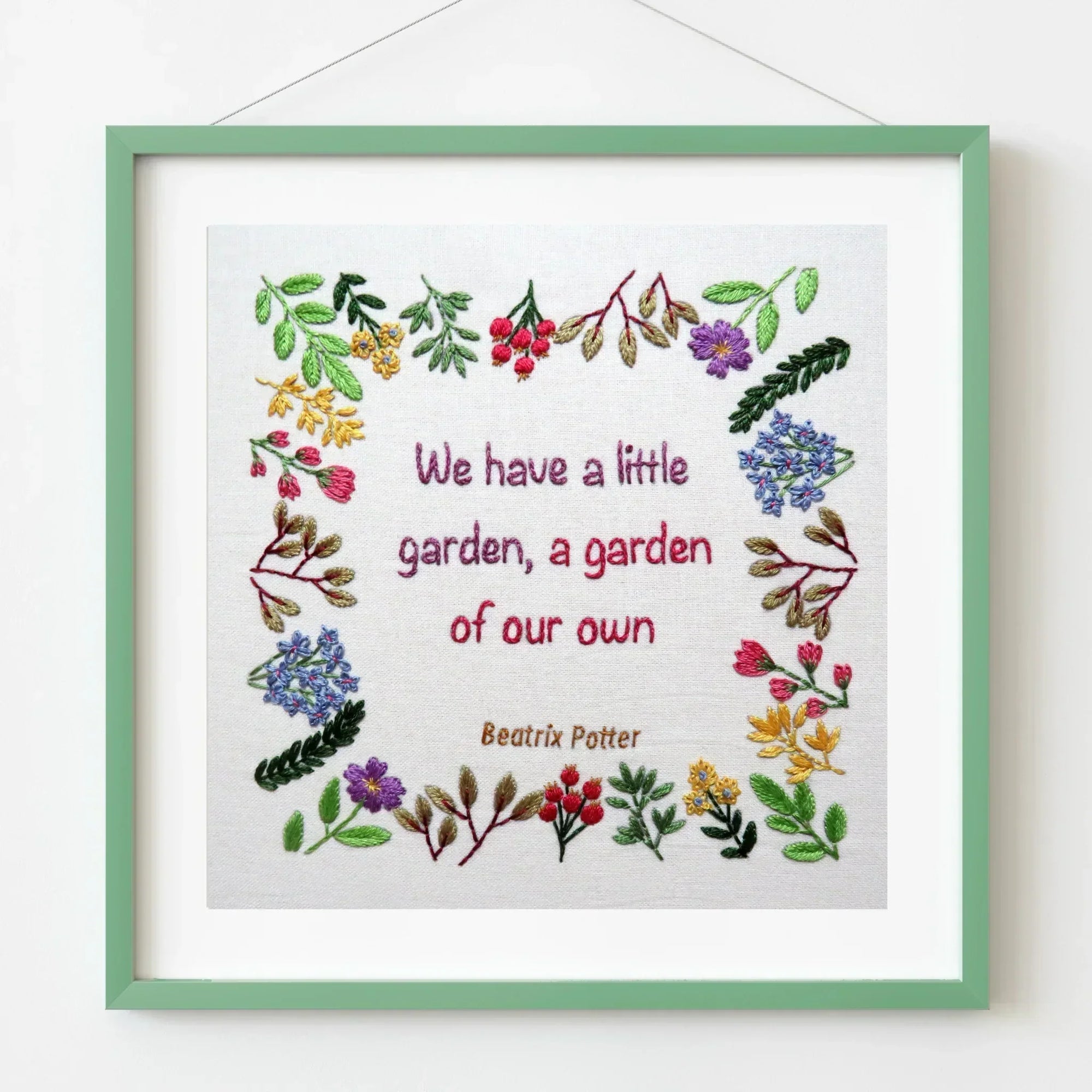Framed embroidery with floral designs and text on a white background