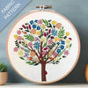 Embroidery hoop with a colorful tree design on fabric, against a gray background.
