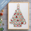 Framed fabric pattern of a Christmas tree with decorative elements on a wooden surface.