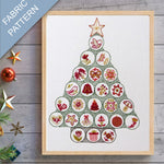 Framed fabric pattern of a Christmas tree with decorative elements on a wooden surface.