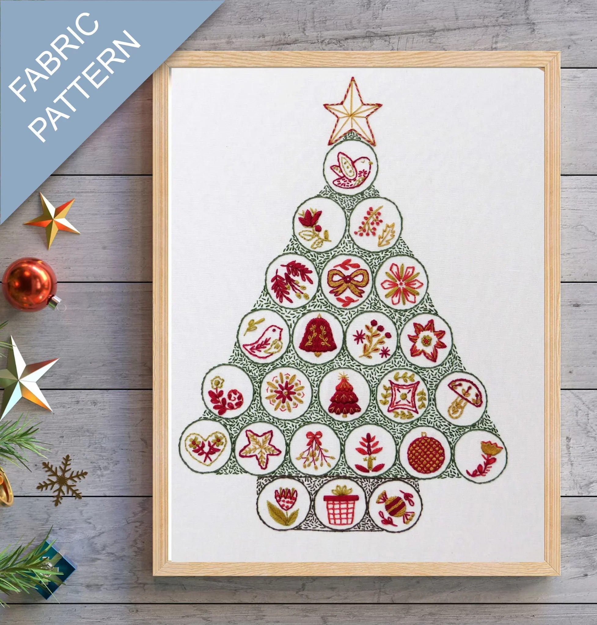 Framed fabric pattern of a Christmas tree with decorative elements on a wooden surface.