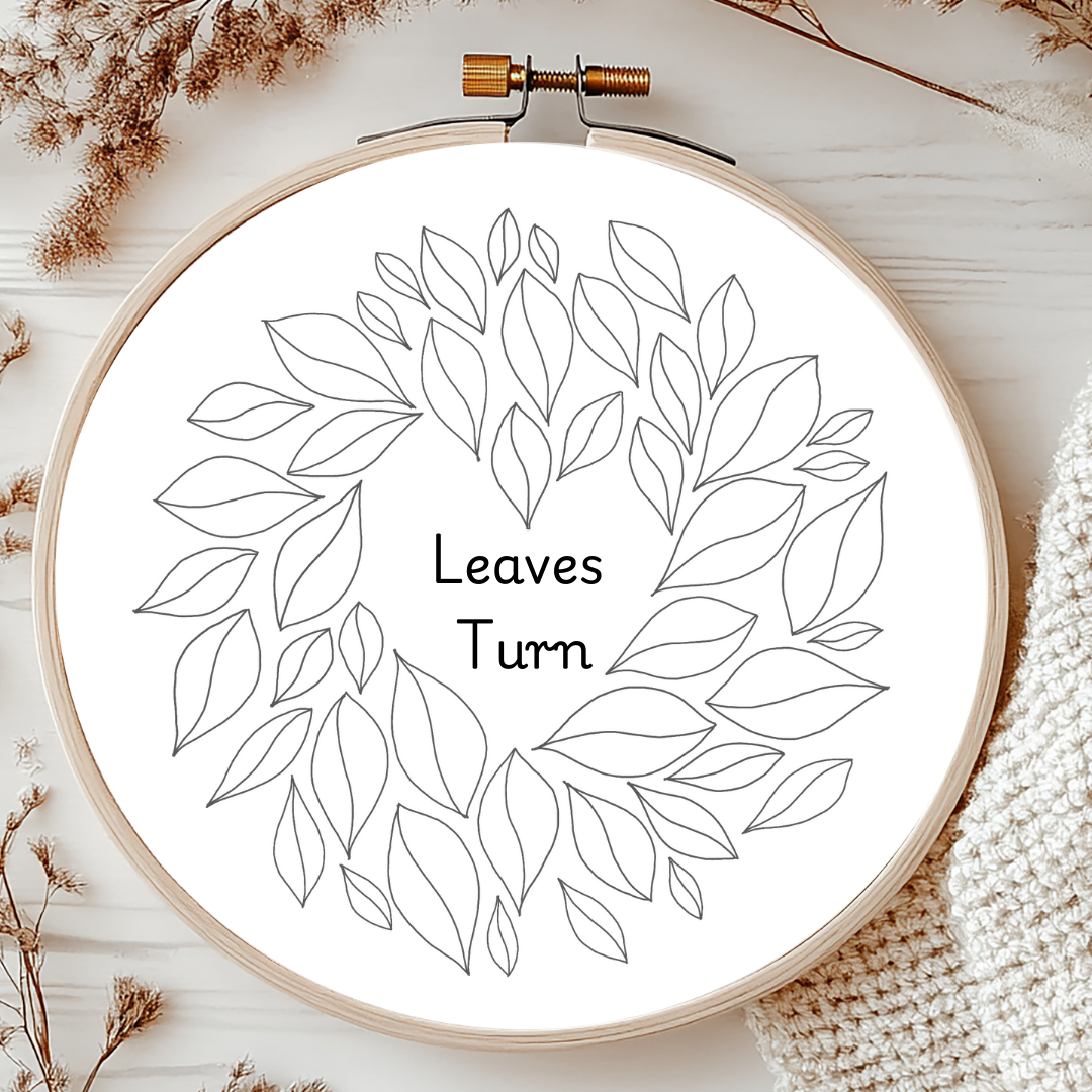 Embroidery hoop with leaf pattern and text 'Leaves Turn' on a wooden surface.