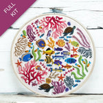 Embroidery hoop with colorful underwater scene including fish, corals, and turtles on a white wooden surface.