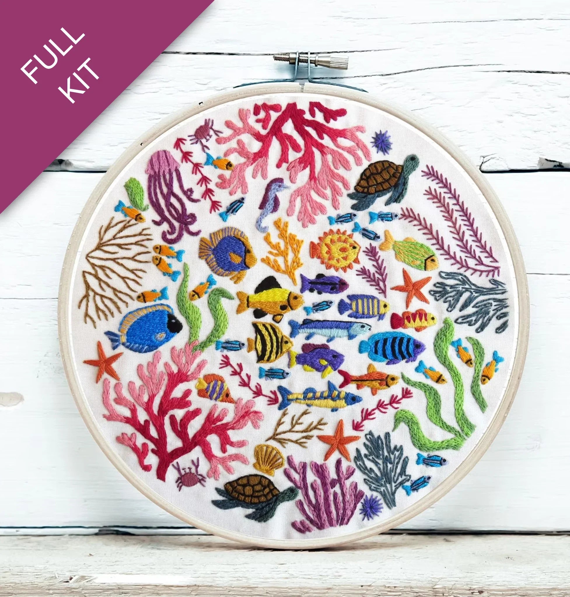 Embroidery hoop with colorful underwater scene including fish, corals, and turtles on a white wooden surface.