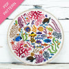 Embroidery hoop with colorful underwater scene including fish, corals, and turtles on a white wooden surface.
