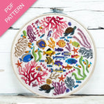 Embroidery hoop with colorful underwater scene including fish, corals, and turtles on a white wooden surface.