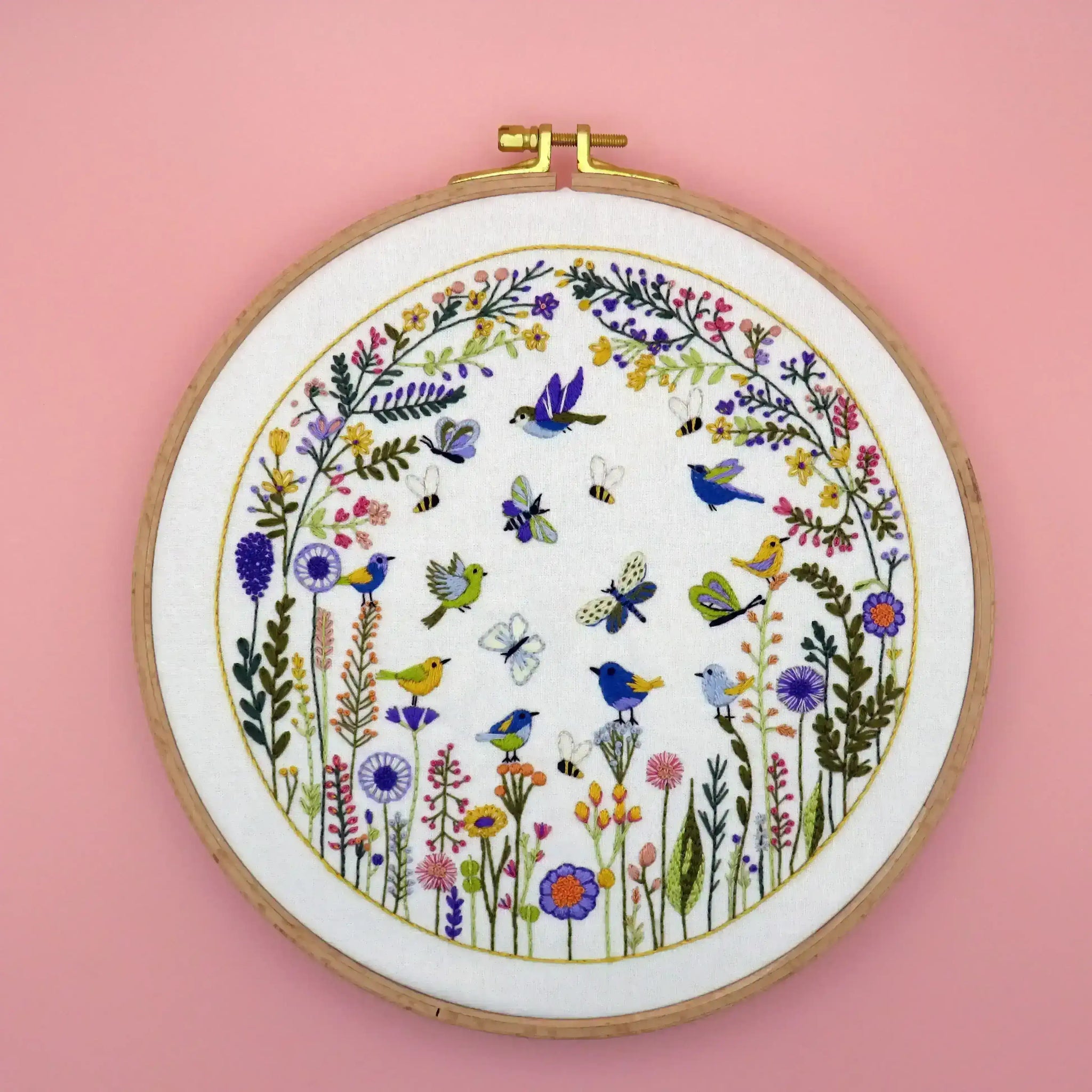 Embroidery hoop with floral and bird design on a pink background