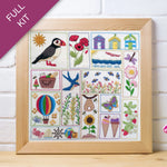 Framed embroidered sampler with various designs including a puffin, flowers, and animals on a white background.