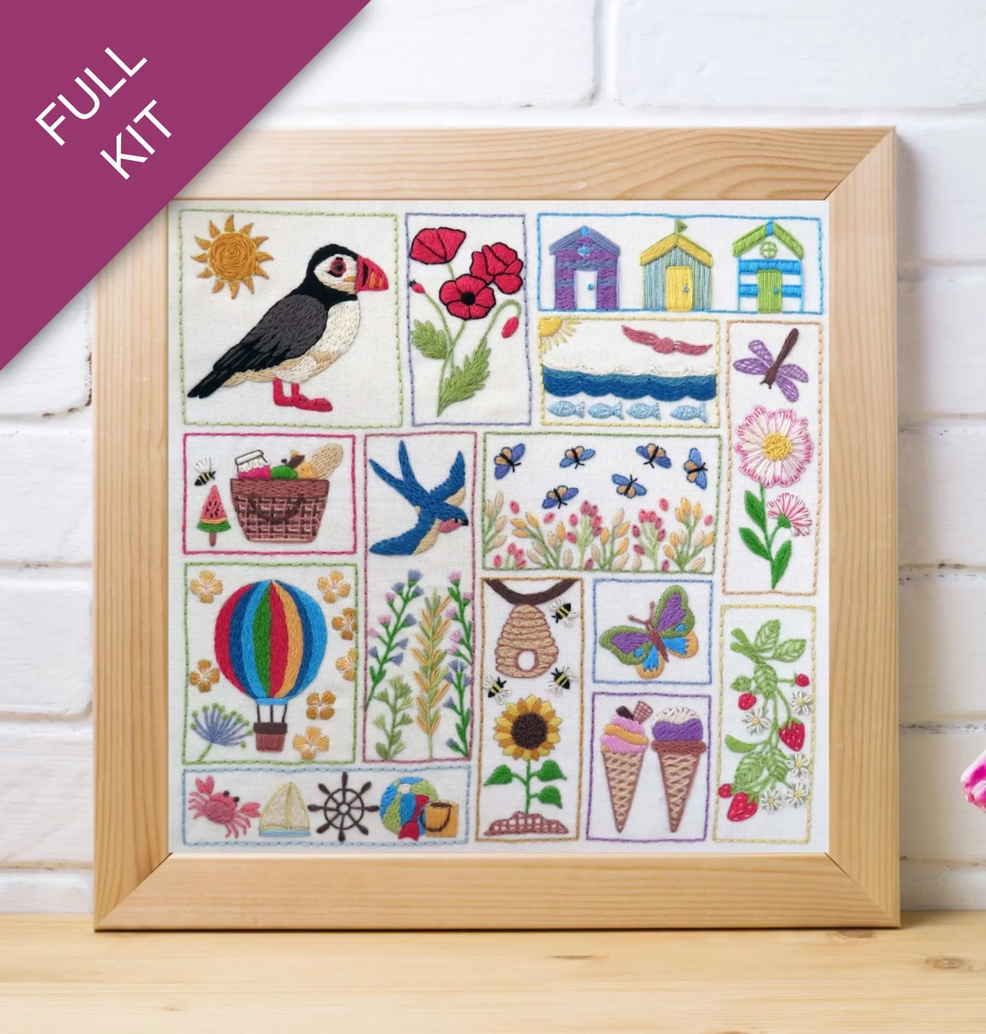 Framed embroidered sampler with various designs including a puffin, flowers, and animals on a white background.