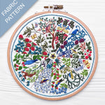 Embroidery hoop with a colorful fabric pattern featuring birds and trees on a white background.