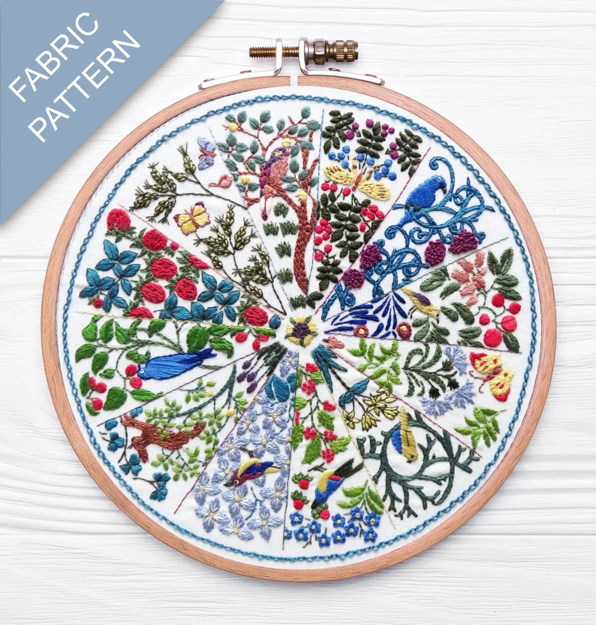 Embroidery hoop with a colorful fabric pattern featuring birds and trees on a white background.