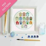 Embroidery kit with colorful beach hut design, thread, and tools on a white background.
