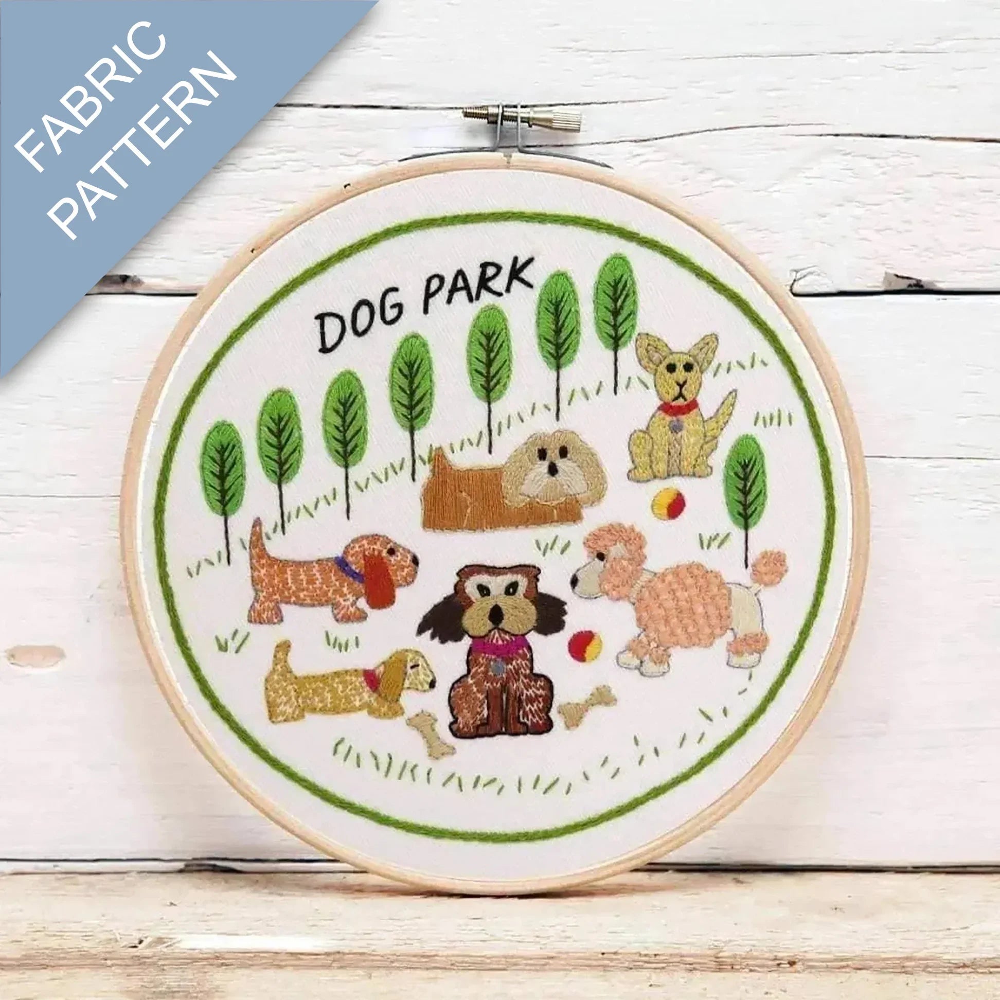 Embroidery hoop with 'Dog Park' design featuring cartoon dogs and trees on a wooden surface.