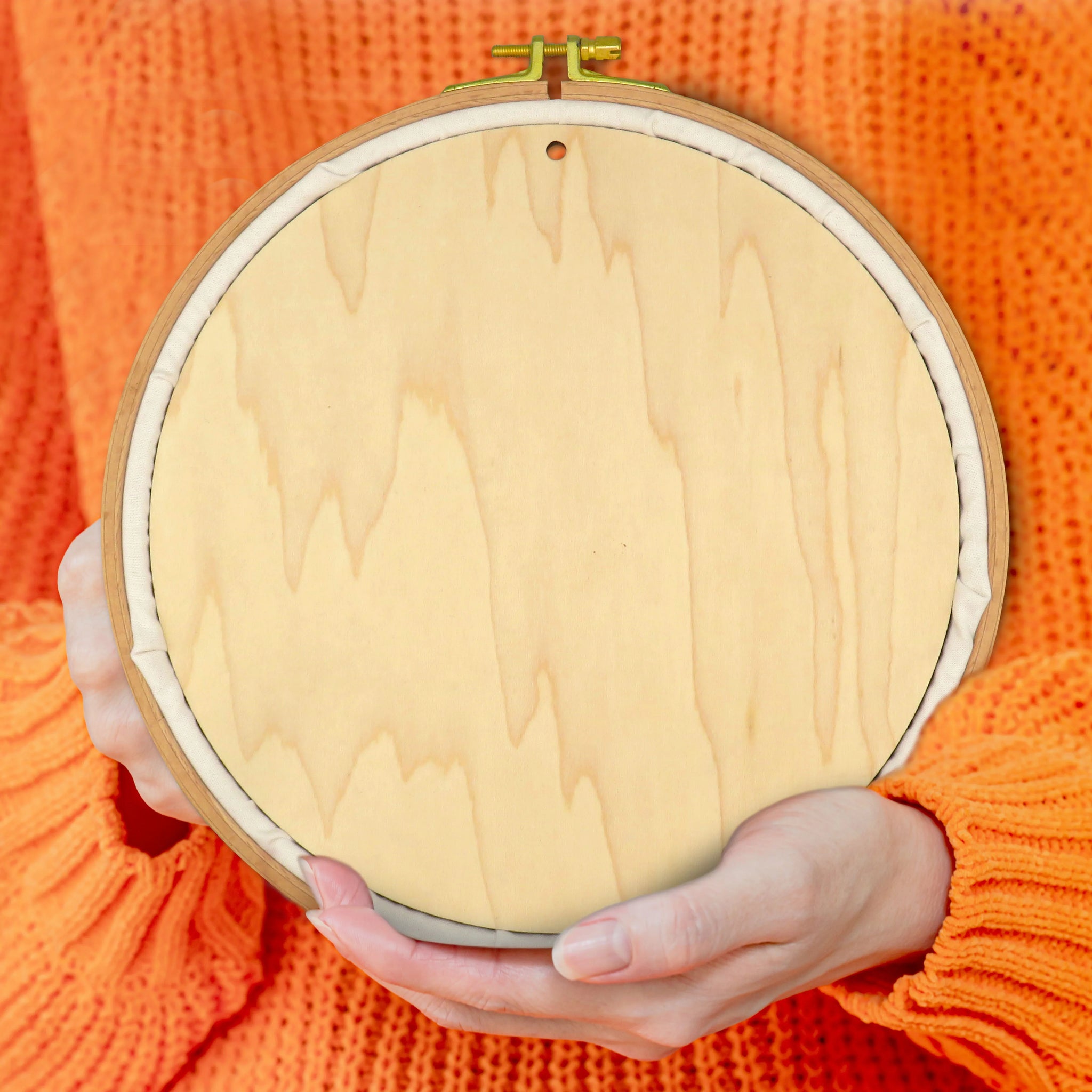 Wooden embroidery hoop held by a person wearing an orange sweater