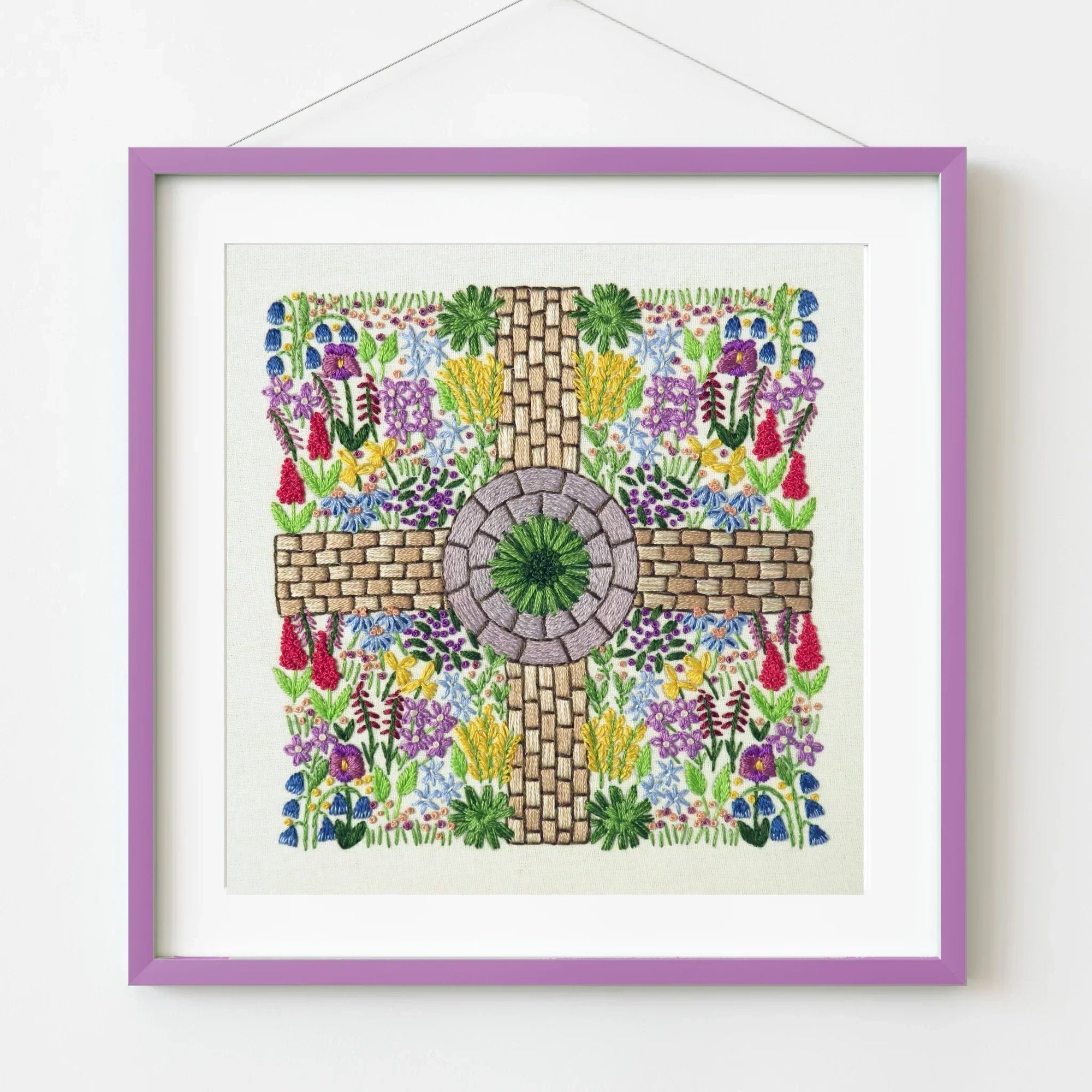 Framed artwork with a cross design surrounded by colorful flowers on a white background