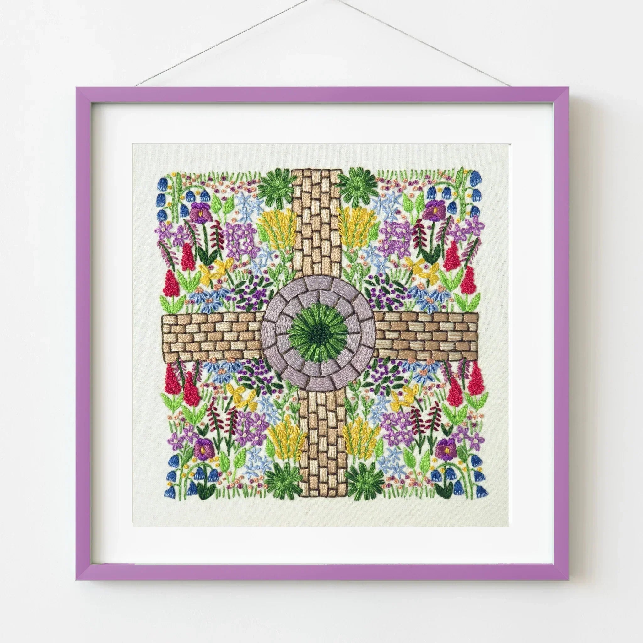 Framed artwork with a cross design surrounded by colorful flowers on a white background