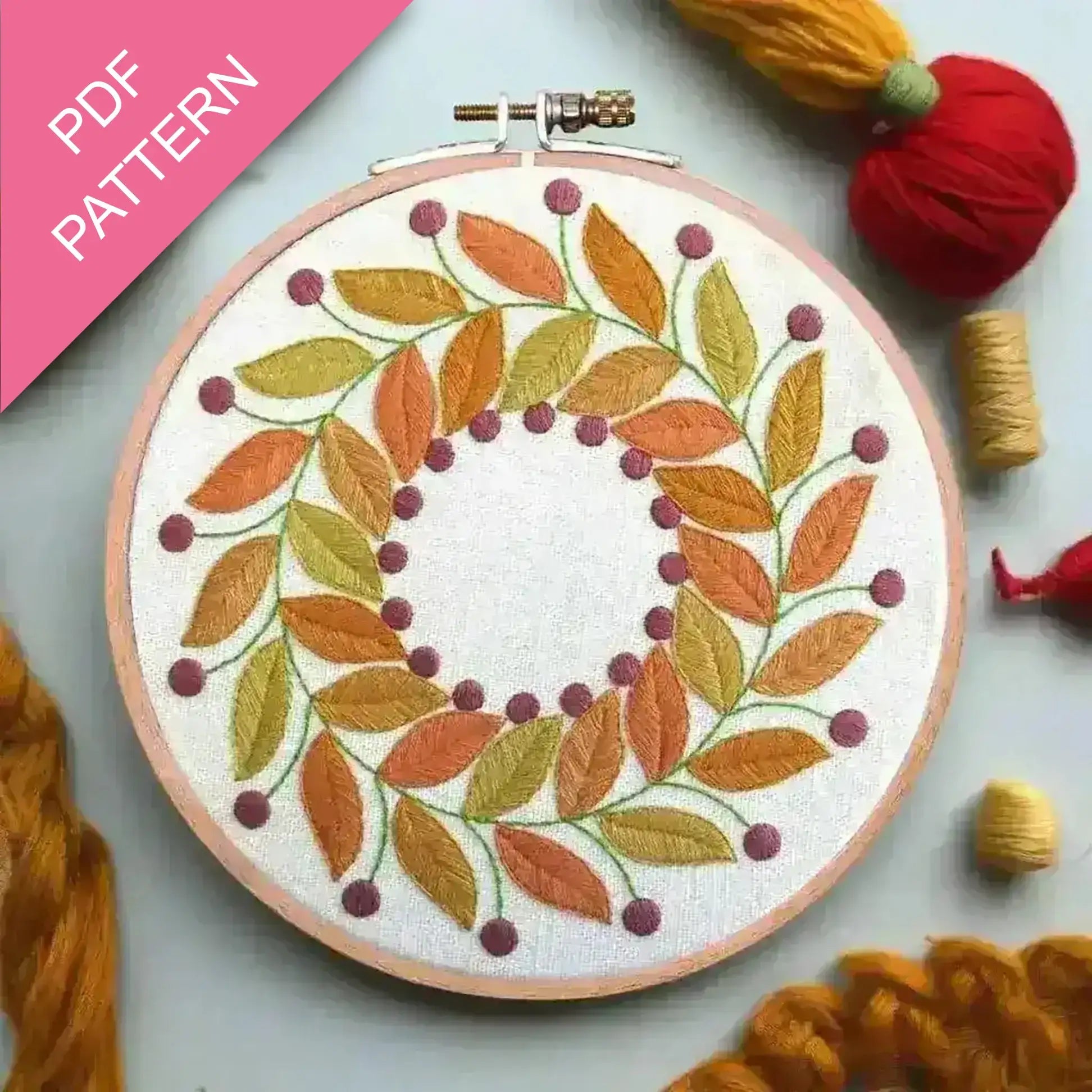 Embroidery hoop with autumn leaf pattern surrounded by yarn on a light background