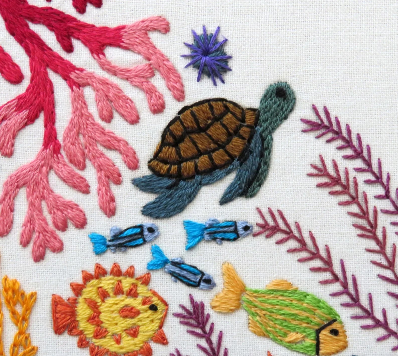 Embroidered design of a turtle, fish, and coral on fabric.