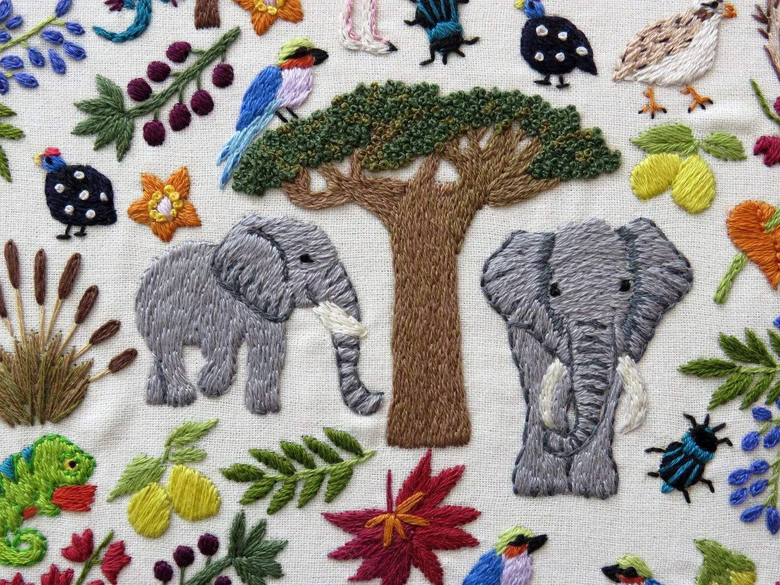 Embroidered scene with elephants, trees, and various animals on a fabric background