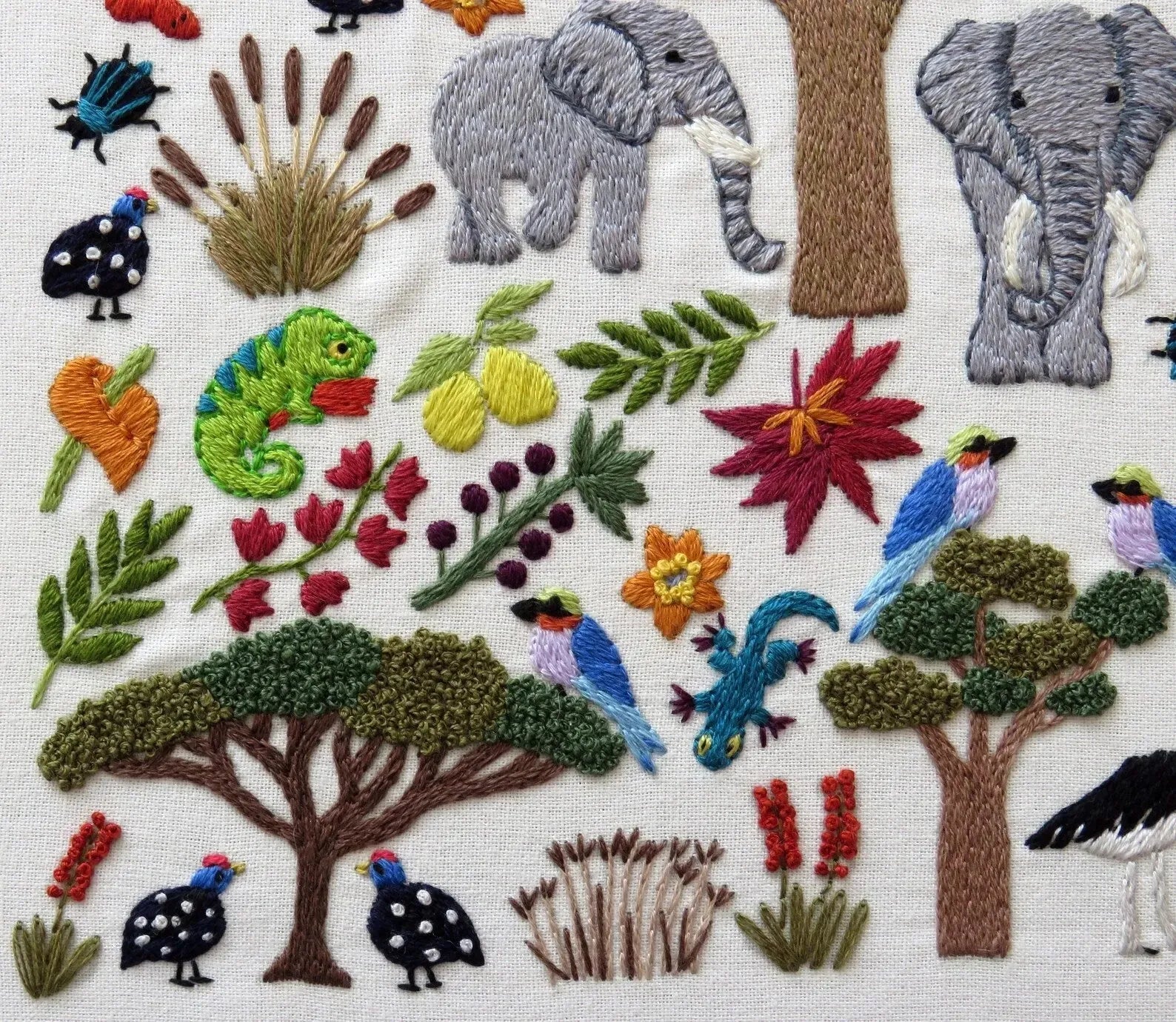 Embroidered scene with elephants, birds, flowers, and trees on a white background