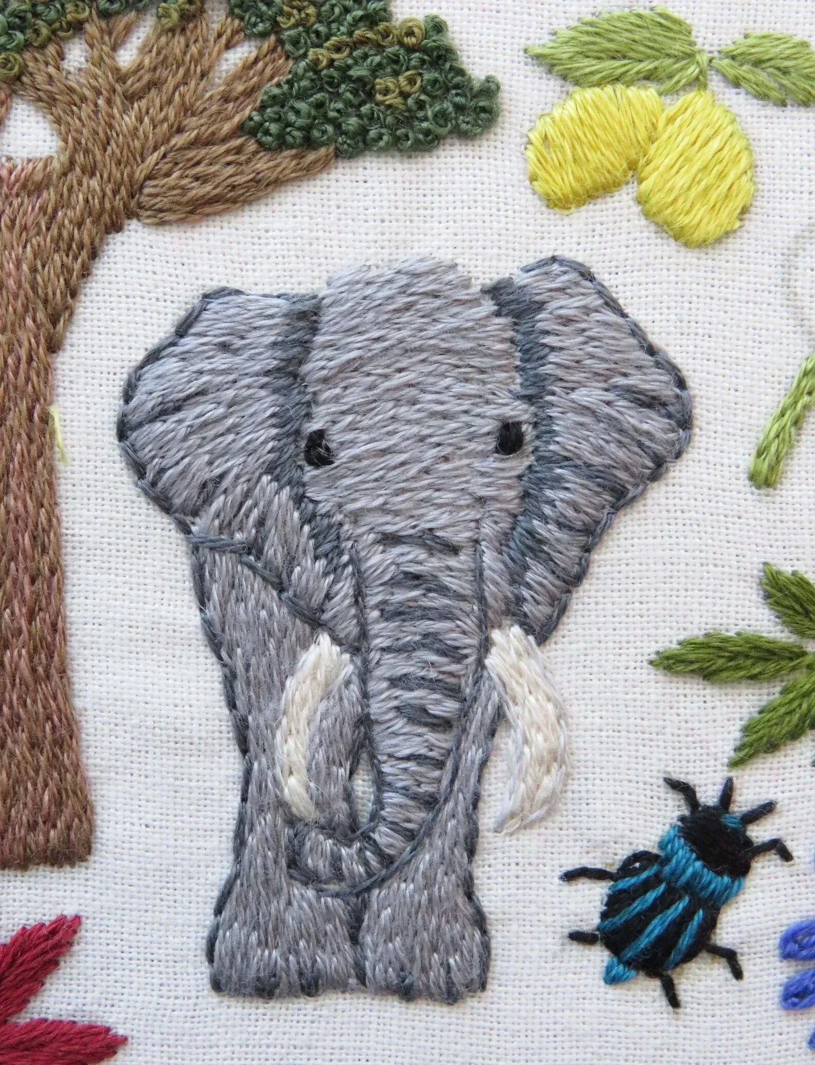 Embroidered design of an elephant surrounded by trees and leaves on a white background