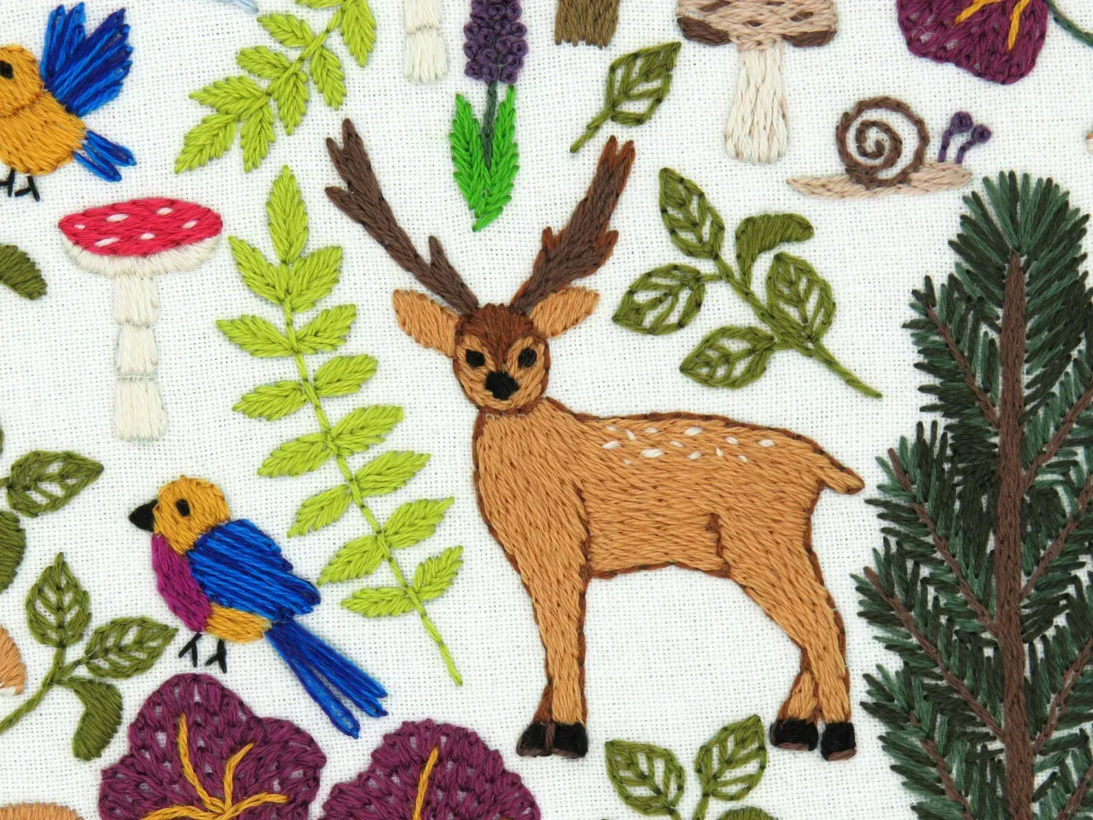 Embroidered fabric with deer, birds, and plants on a white background