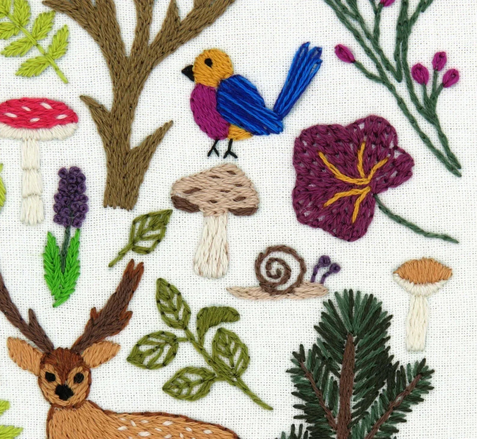 Embroidered design with deer, flowers, mushrooms, and plants on a white background