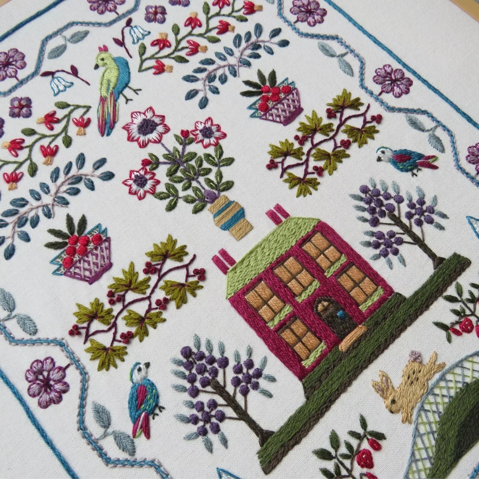 Embroidered design of a house, birds, and flowers on a white background