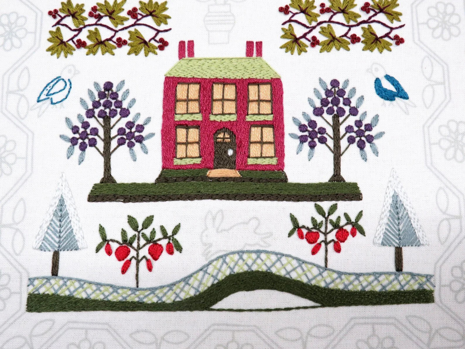 Embroidered design of a house with trees and birds on a white background