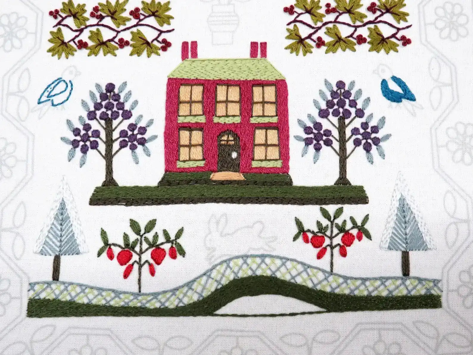 Embroidered design of a house with trees and birds on a white background
