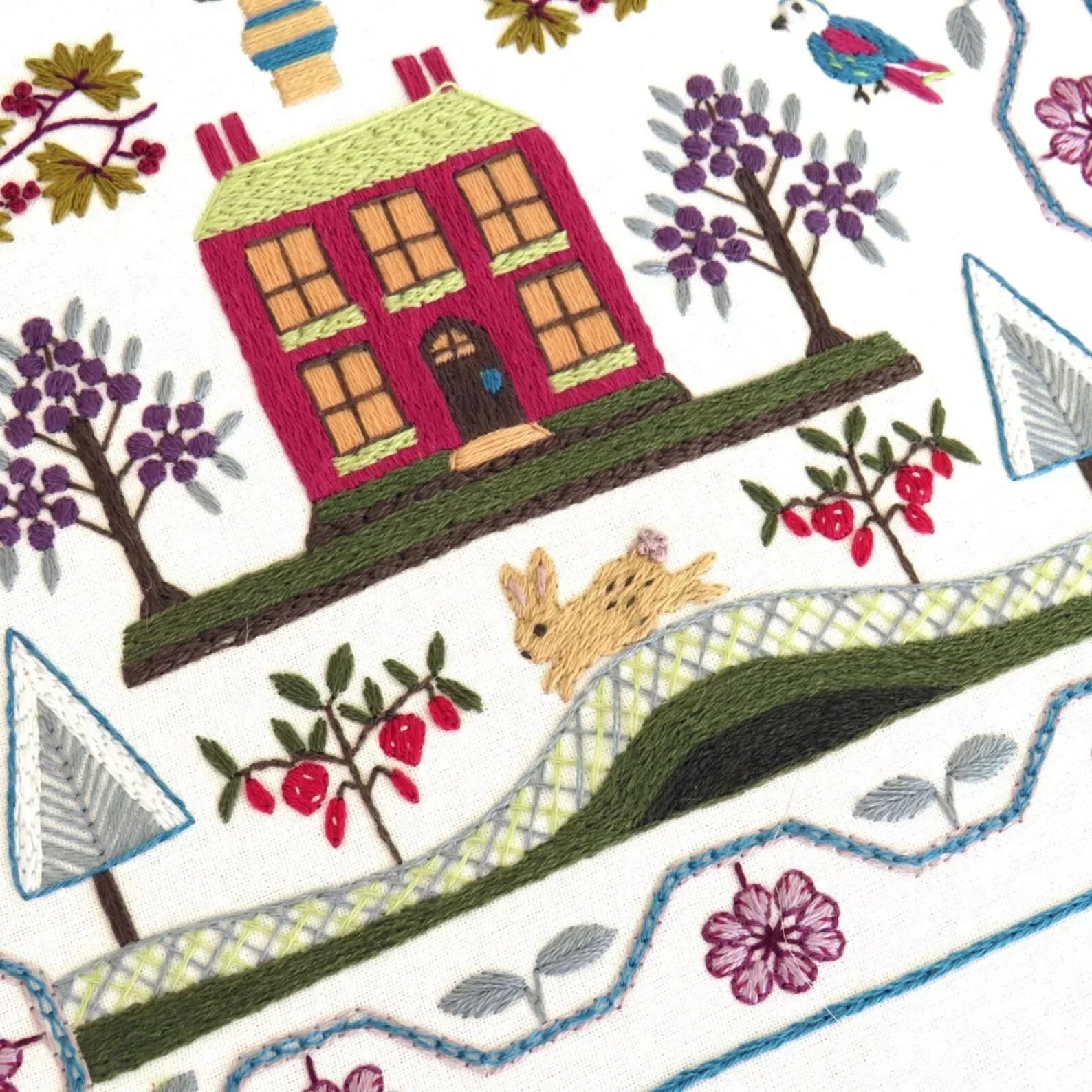 Embroidered design of a house, trees, and a rabbit on a white background