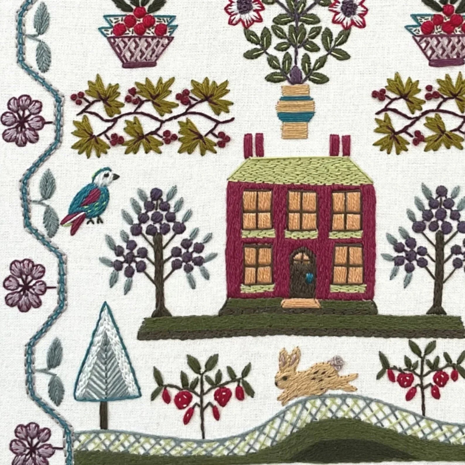 Embroidered design of a house, trees, and animals on a white background