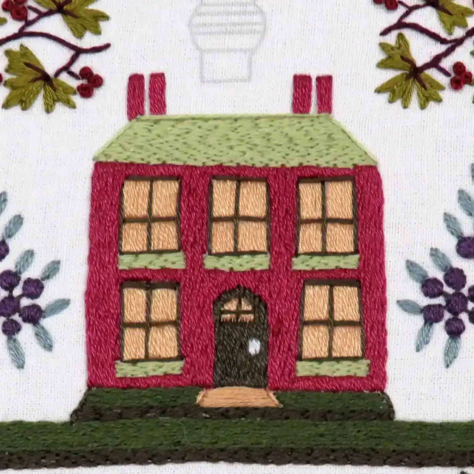 Embroidered design of a house with windows and a door, surrounded by foliage.