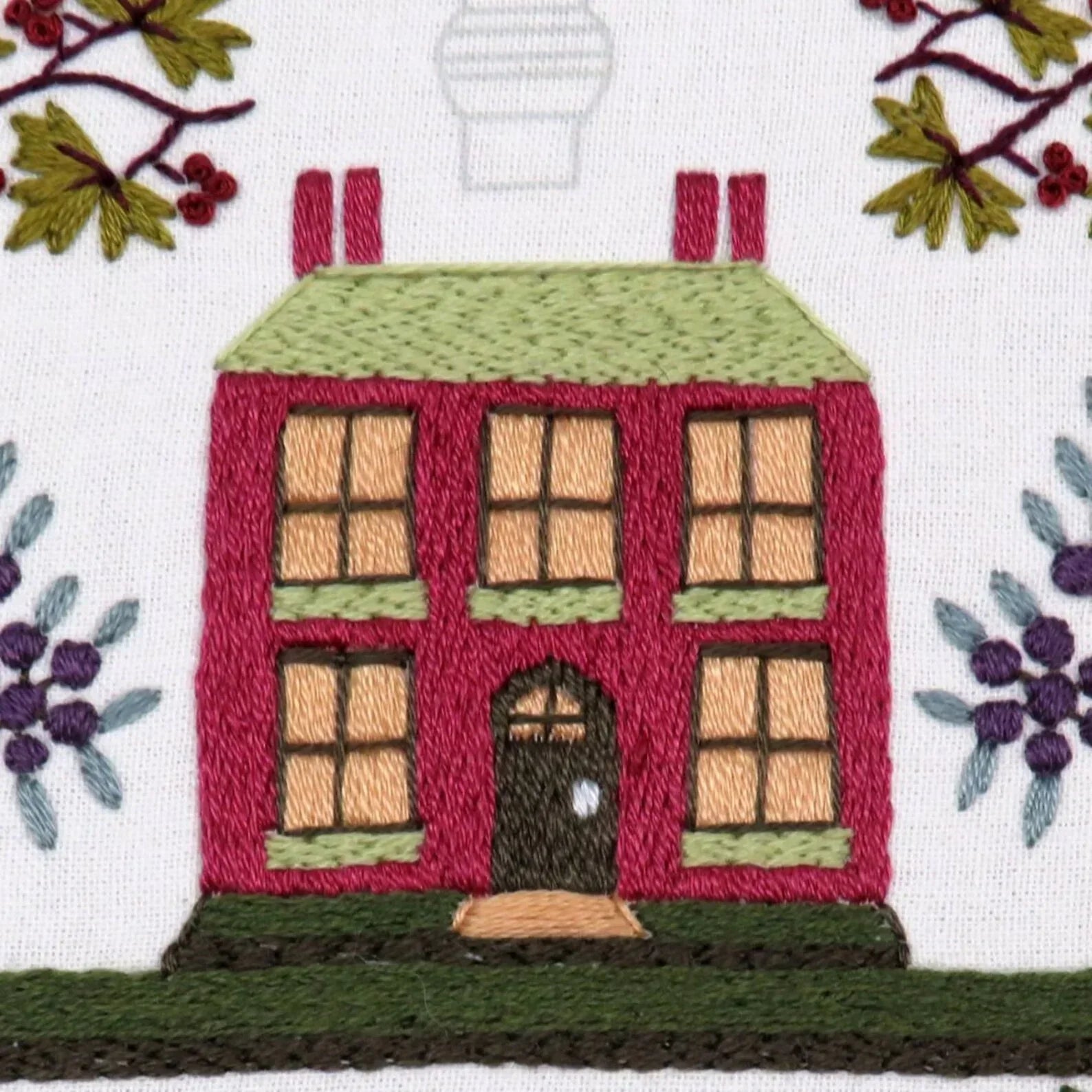 Embroidered design of a house with windows and a door, surrounded by foliage.