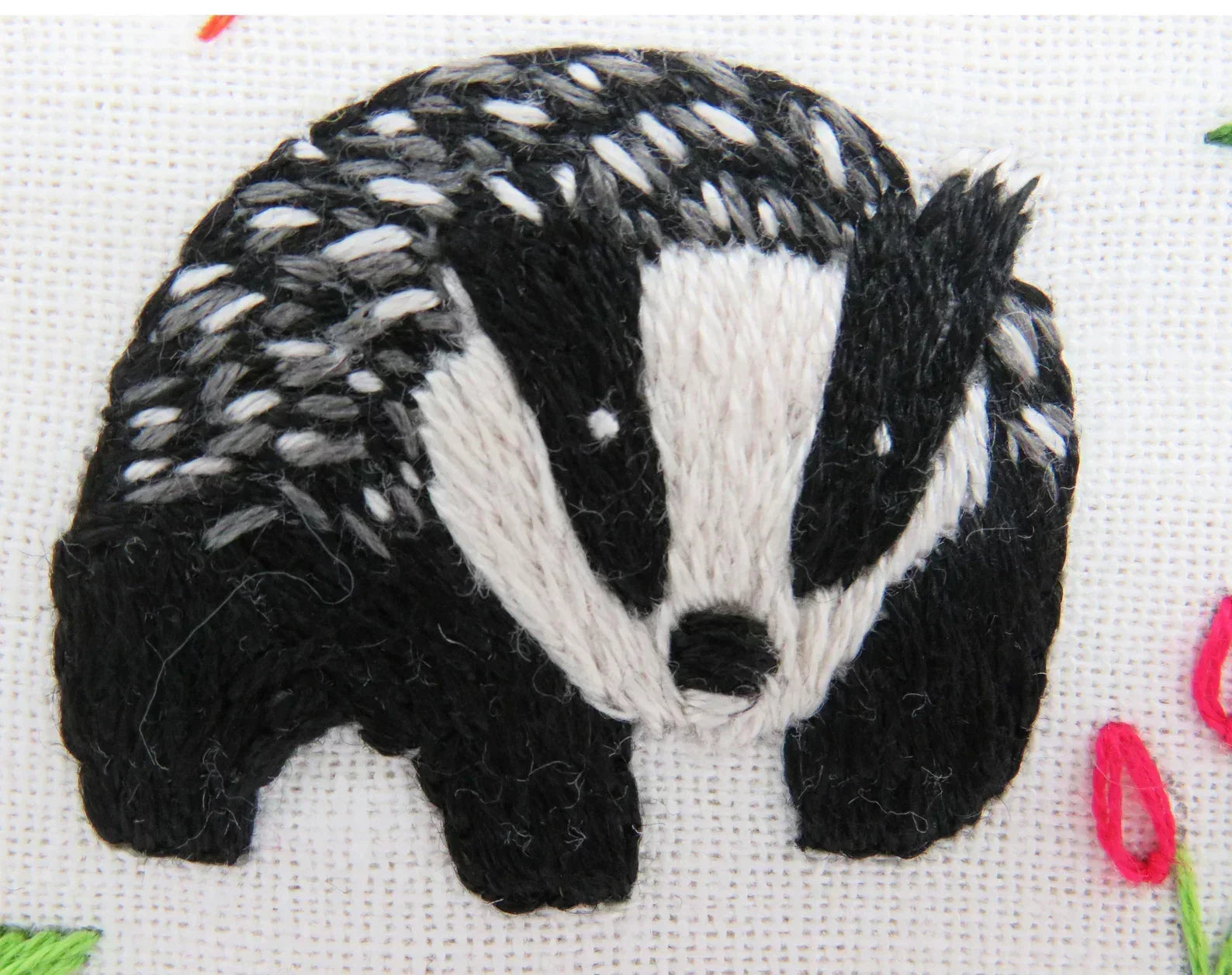 Embroidered badger design on fabric with a cross-stitch pattern.