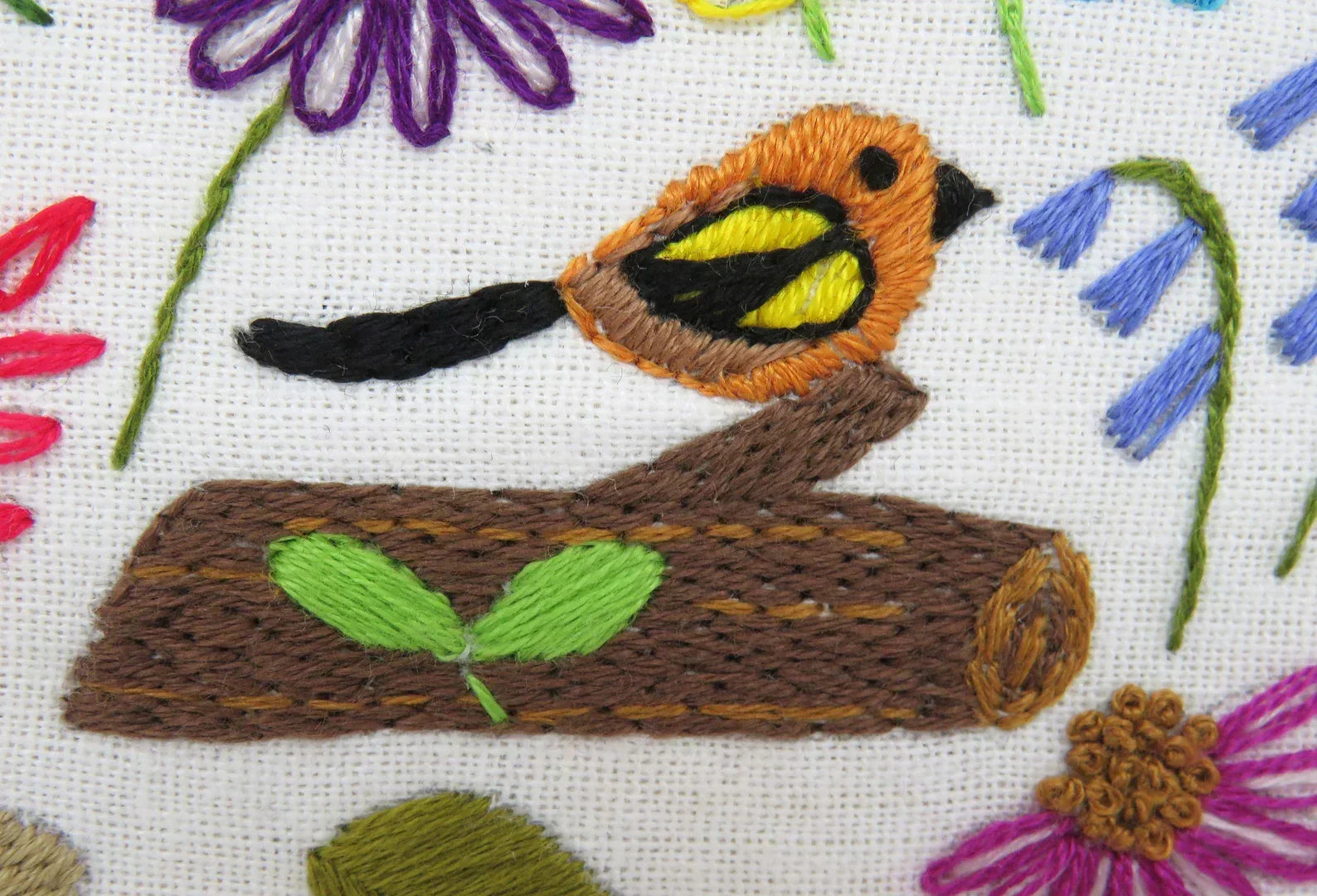 Embroidered design of a bird on a log with flowers in the background