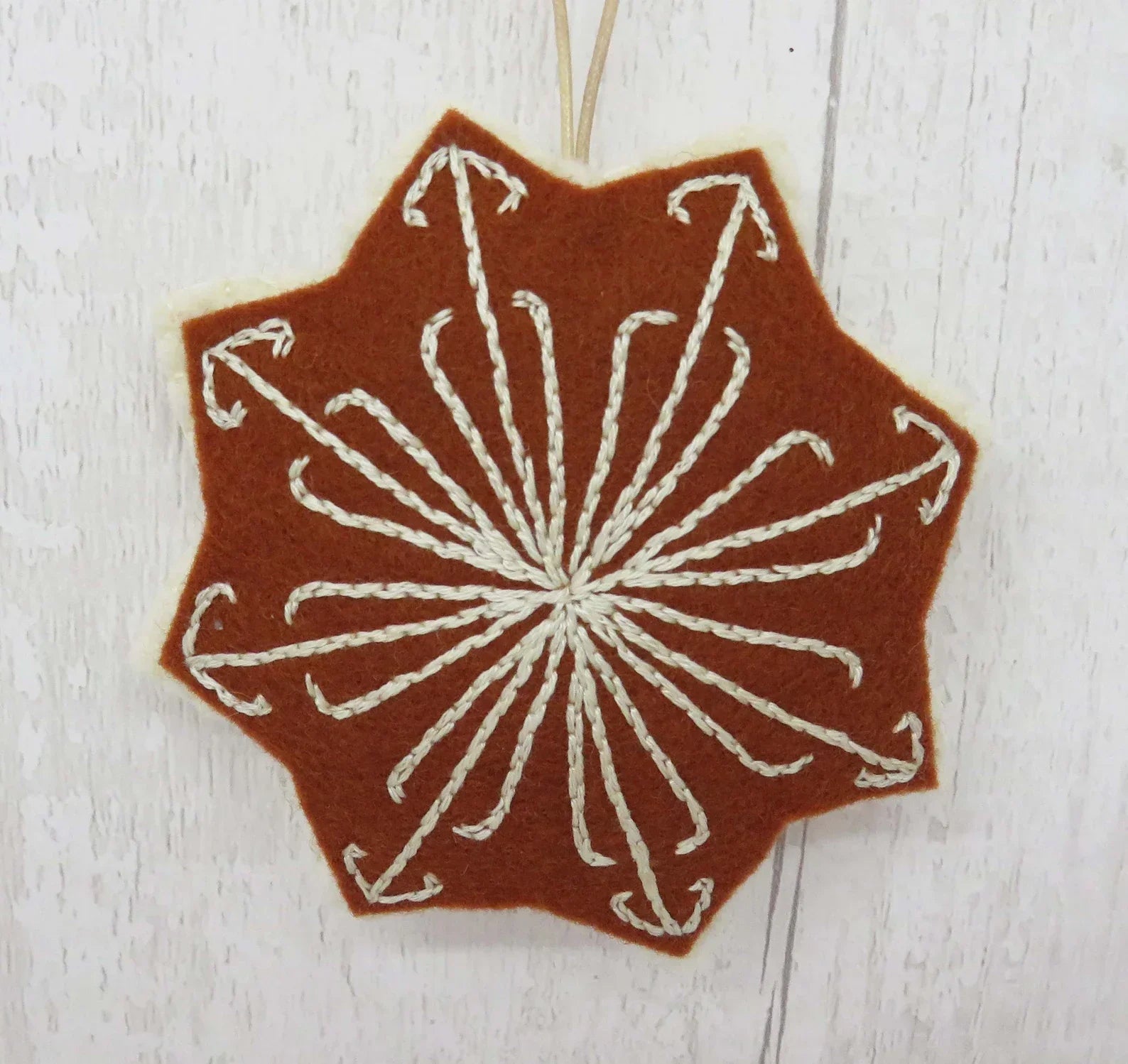 Decorative brown fabric patch with white embroidered pattern on a wooden surface