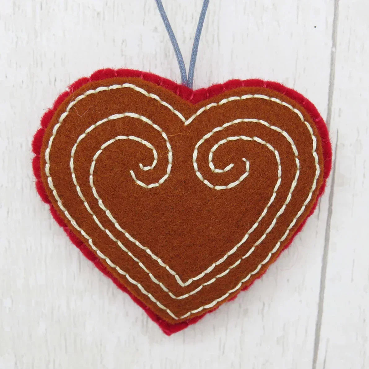 Heart-shaped ornament with brown fabric and white stitching on a light wooden background