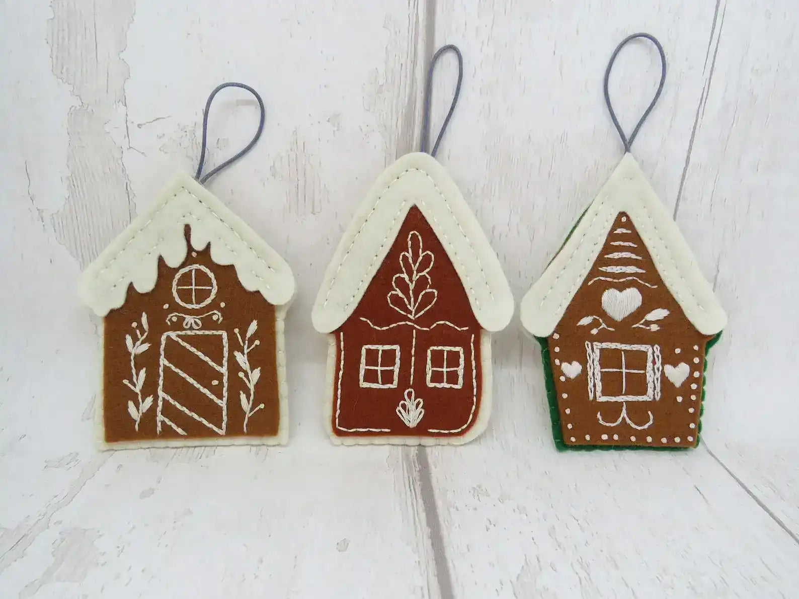Three gingerbread house-shaped ornaments on a wooden surface
