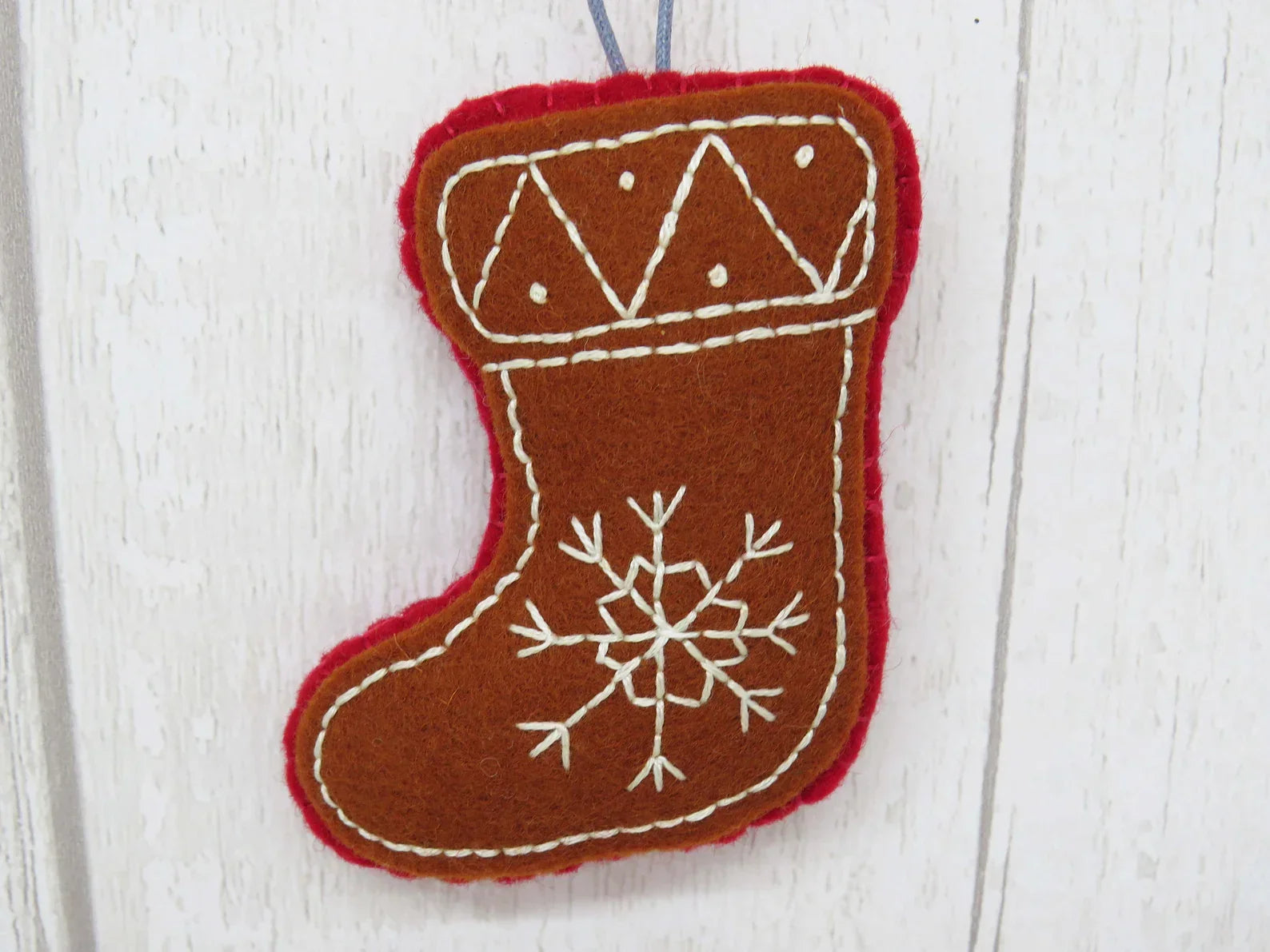 Felt Christmas stocking ornament with snowflake design on a white wooden background
