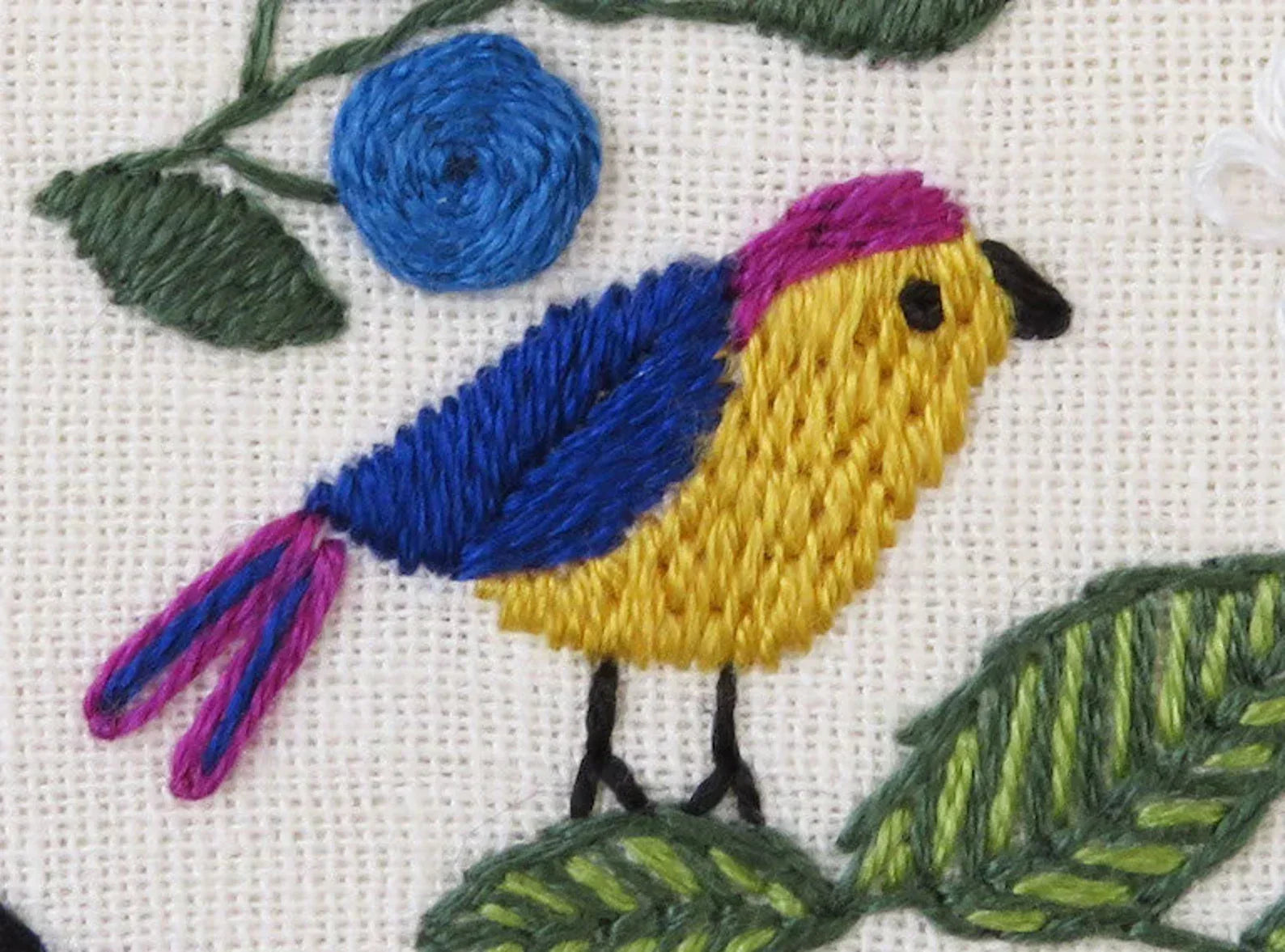 Embroidered design of a bird with blue, yellow, and pink colors on a white background.