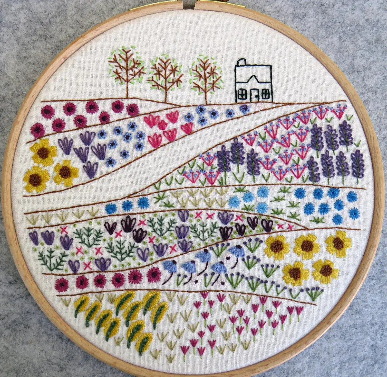 Embroidery hoop with floral and landscape design on a gray background