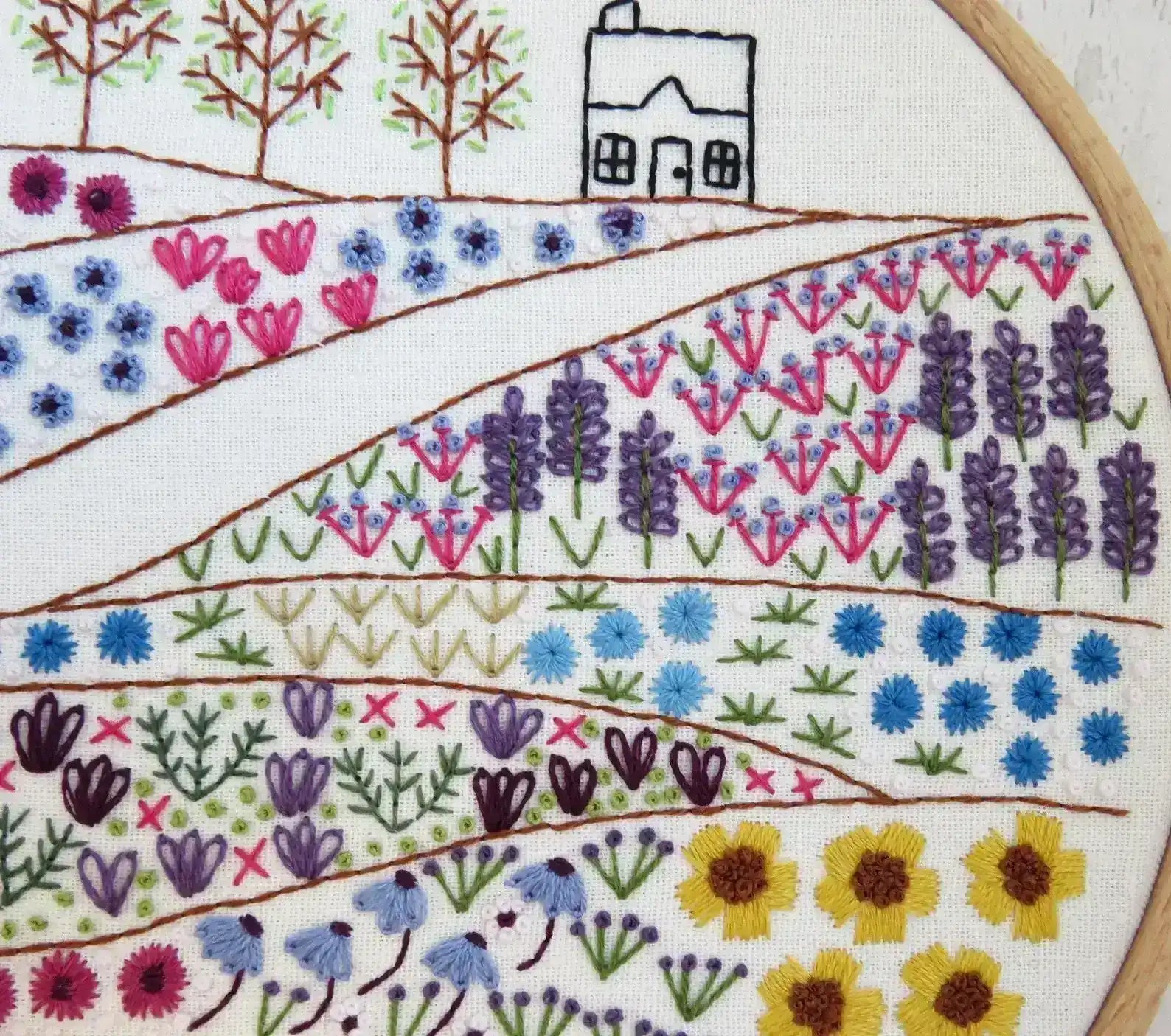 Embroidery hoop with a colorful floral and landscape design.