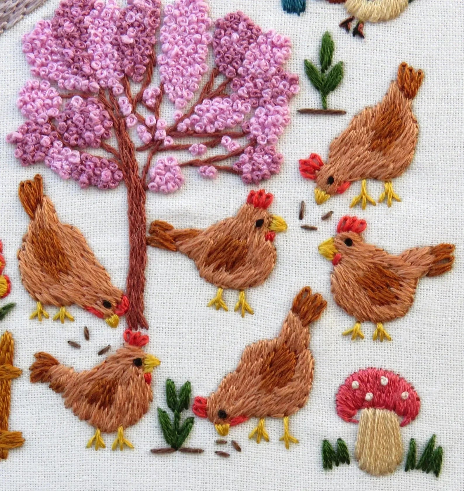 Embroidery of chickens around a pink flowering tree with mushrooms.