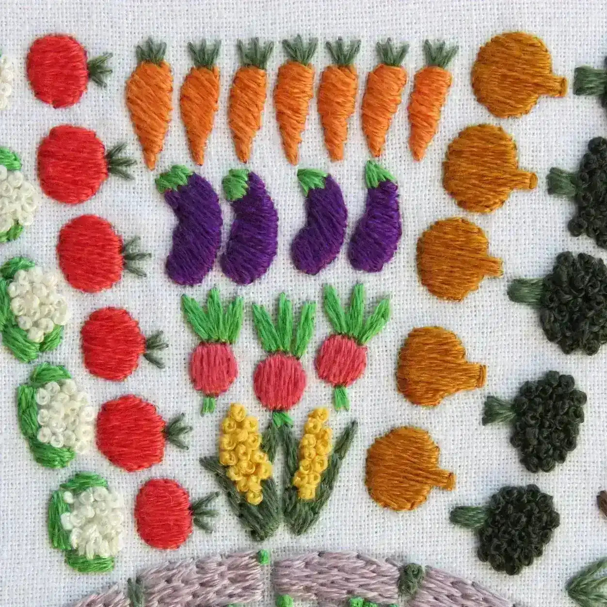 Embroidered vegetables including carrots, eggplants, and tomatoes on a white background