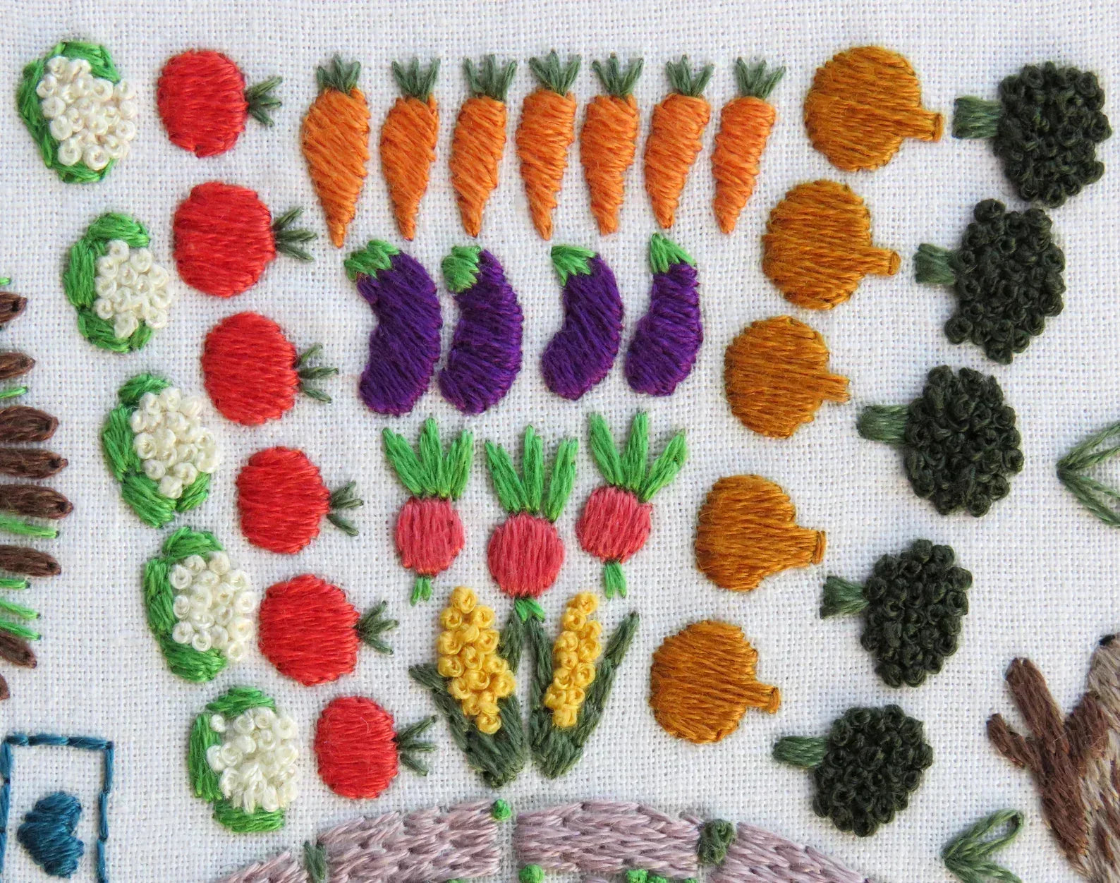 Embroidered vegetables including carrots, eggplants, and tomatoes on a white background