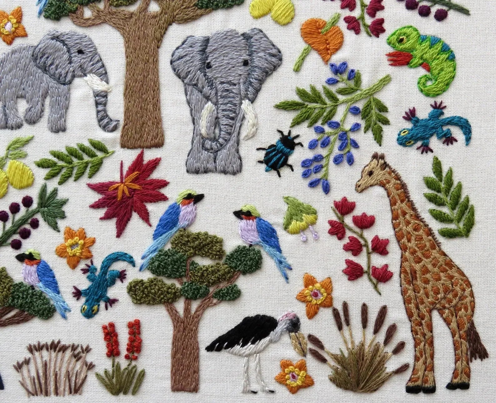 Embroidered scene with elephants, giraffes, birds, and flowers on a white background